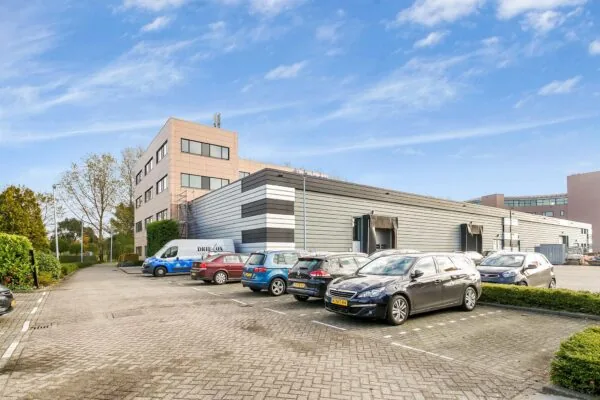 Bedrijventerrein aan de Laan van ‘s-Gravenmade met een modern kantoorgebouw, bedrijfsruimte en geparkeerde auto's.